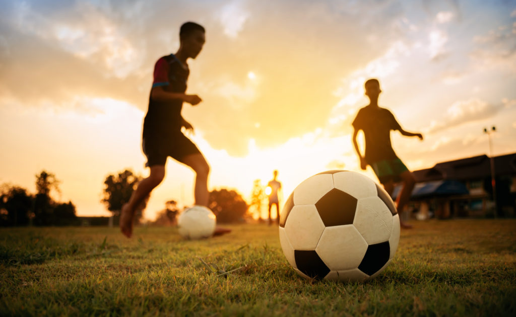 group of kids having fun playing soccer football for exercise in community rural area under the twilight sunset sky