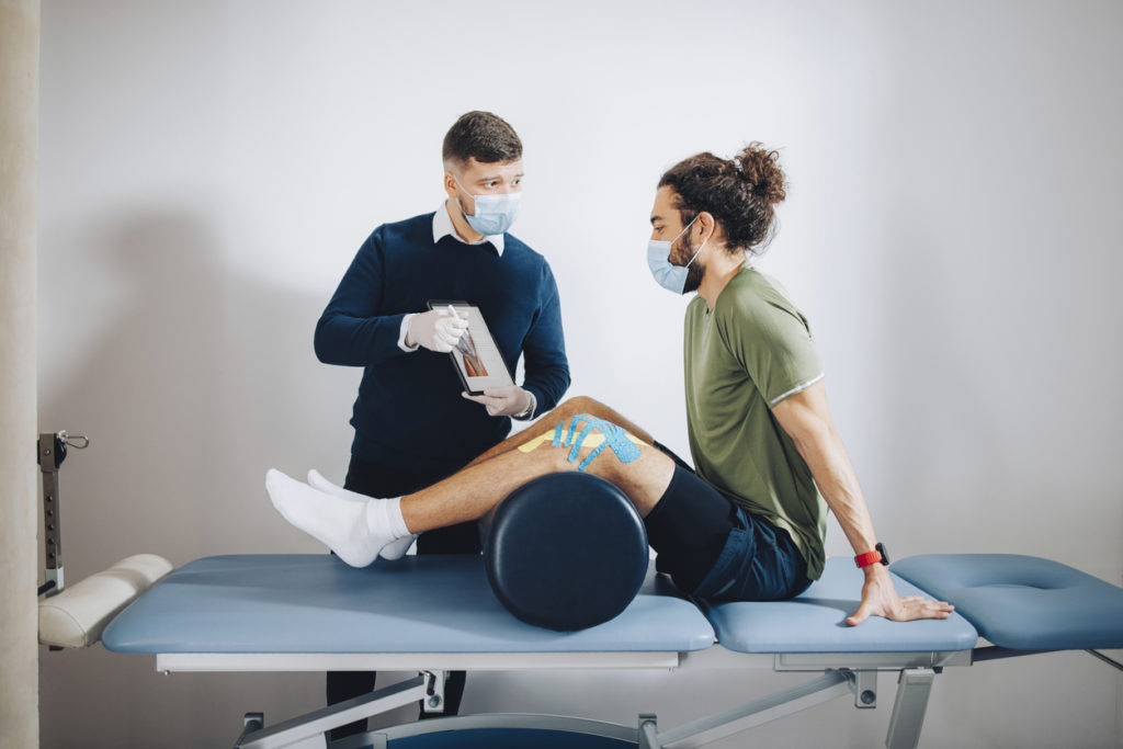 Sport Medicine Doctor Holding an Anatomy Chart and Explaining the Problem to the Patient