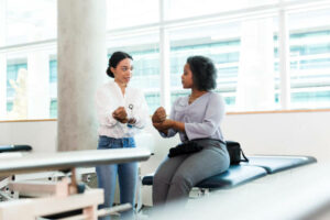 A female physical therapy patient bends her injured wrist while listening and watching a physical therapist.