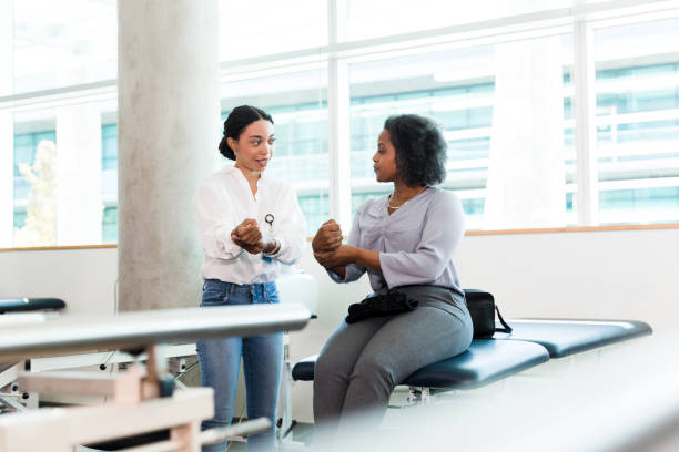 A female physical therapy patient bends her injured wrist while listening and watching a physical therapist.