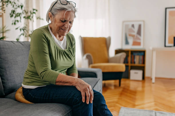 Senior women is suffering from leg and knee pain, sitting on sofa at home