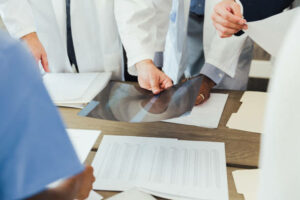 An unrecognizable group of healthcare professionals examine a patient's x-ray during meeting.