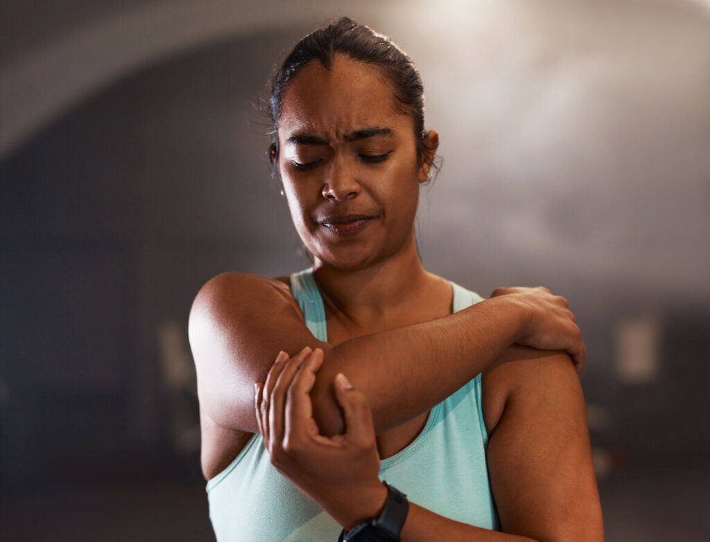 Shot of a young woman experiencing pain from an elbow fracture while working out in a gym.