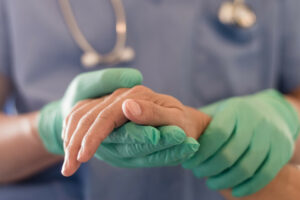 A close-up image of a hand surgeon holding a patient's hand during a surgical operation.