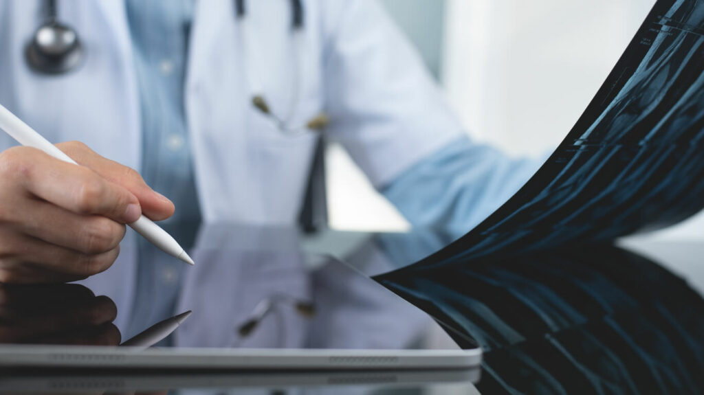 Orthopedic surgeon using a digital tablet to examine and record a patient's knee joint X-ray films.