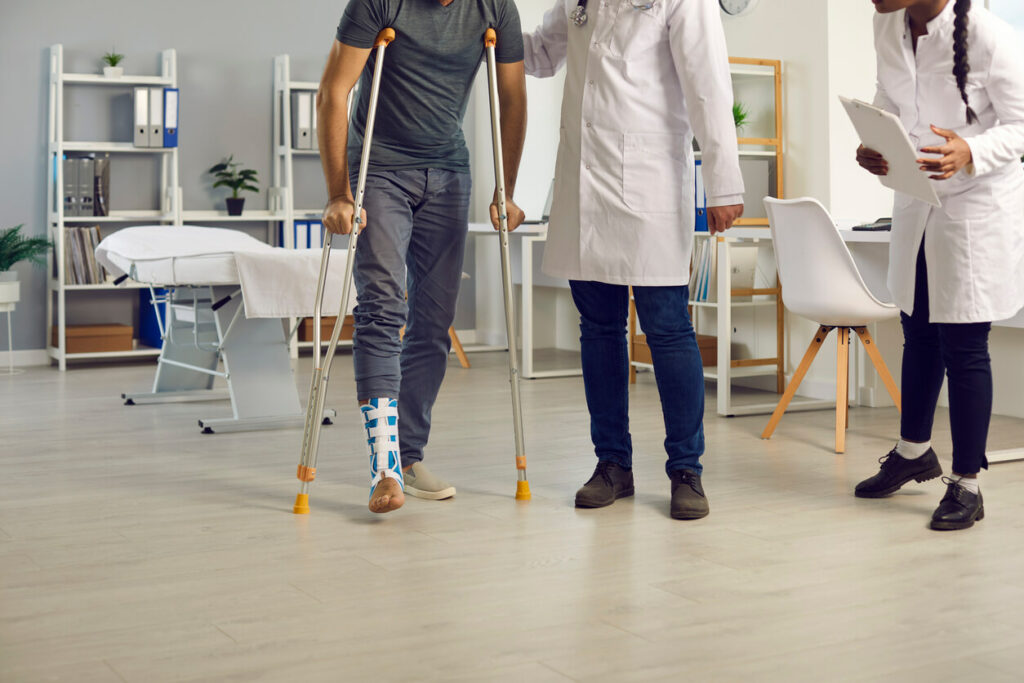 A patient with a leg injury is walking with crutches, assisted by a professional orthopedic surgeon at an orthopedic clinic.