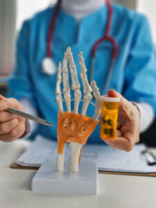 A hand specialist demonstrates an anatomical model of the hand while alongside prescription medication.