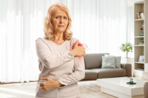 Image of a mature woman in a living room holding her shoulder due to pain from a dislocated shoulder.
