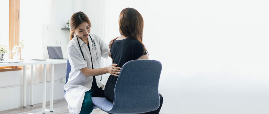 A female orthopedic doctor is diagnosing female patient with back pain in examination room at hospital.