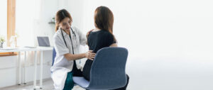 A female orthopedic doctor is diagnosing female patient with back pain in examination room at hospital.