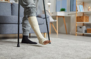 An African American man recovering from a fractured leg uses crutches to move around inside his home.