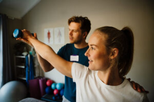 Male sports medicine doctor assists female patient holding arm while raising weight for shoulder rehabilitation