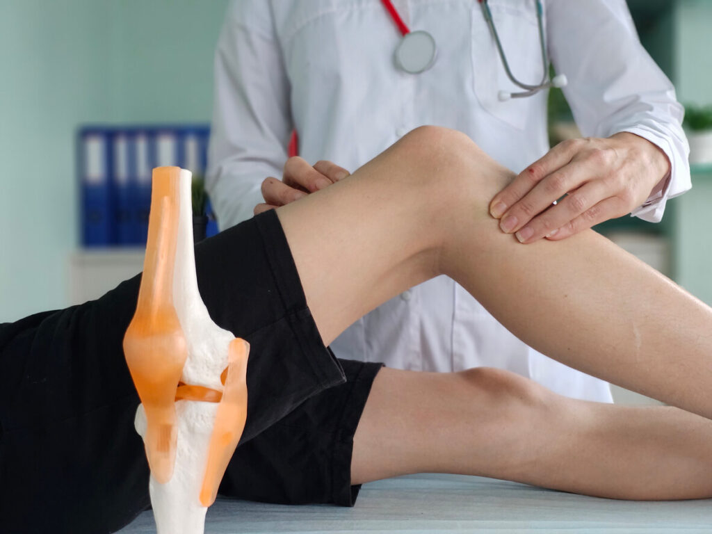 A orthopedic doctor examines the knee of a teenager sitting on an examination
